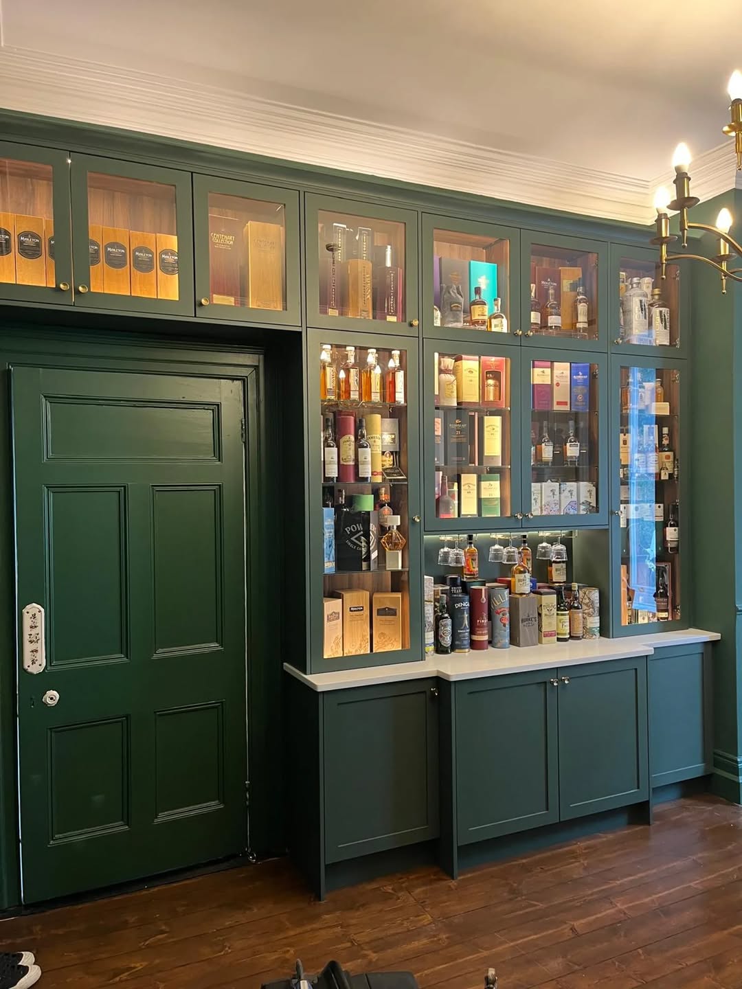 Green fitted home bar and display cabinetry with warm lighting.