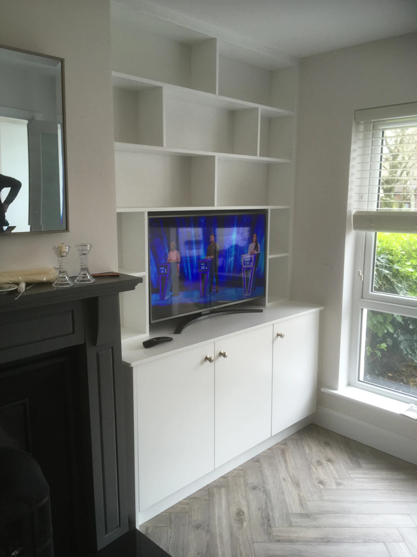 White fitted TV media wall with storage cabinets and display shelving.