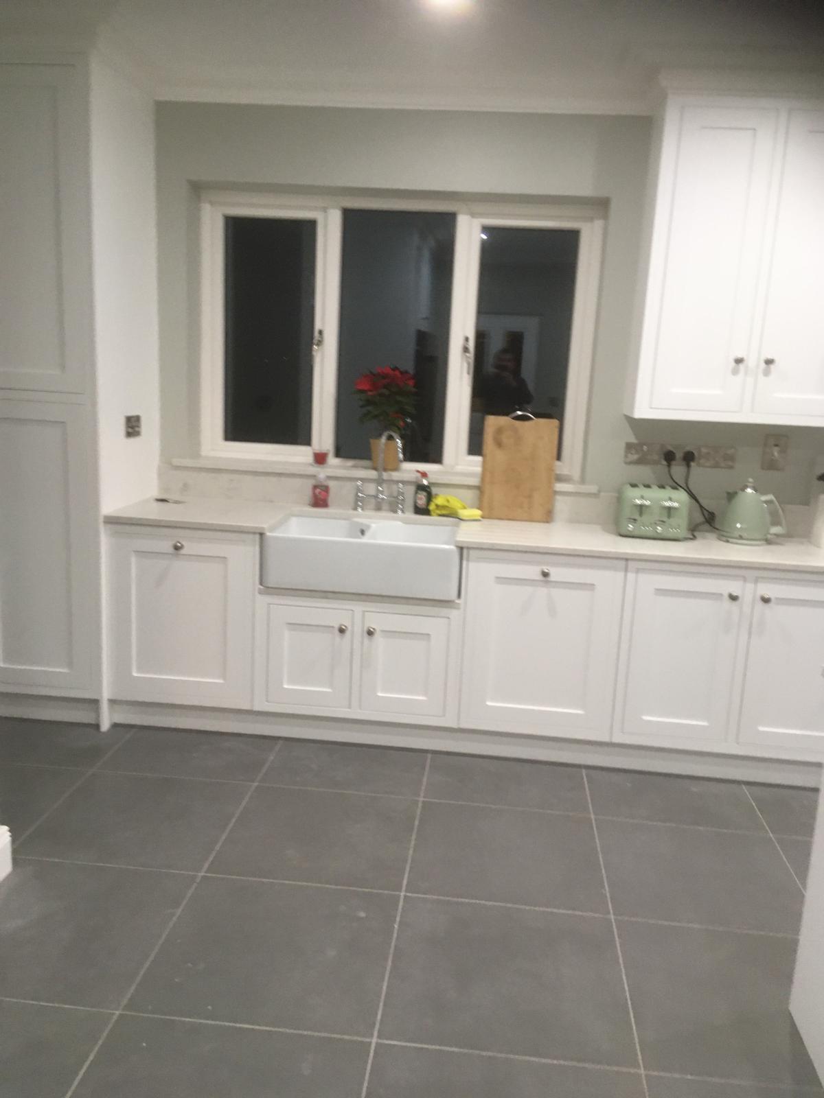 Cream kitchen sink run with farmhouse sink and fitted storage beneath a window.